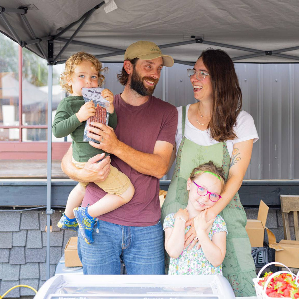 Family of four standing under a tent with food displays in the background